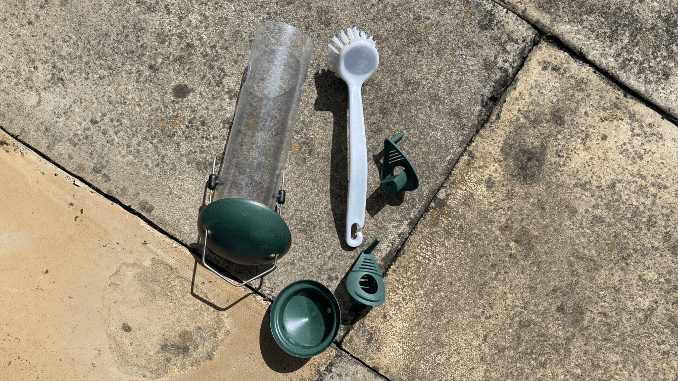 Parts of a bird feeder spread out across the floor with a scrubbing brush for cleaning them